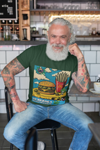 Ein älterer Mann mit weißen Haaren, langem Bart und tätowierten Armen sitzt lächelnd in einem Café. Er trägt ein dunkelgrünes T-Shirt von Temple of Green Elixir, das ein Cartoon-Motiv eines Hamburgers mit Cannabis-Knospen und Pommes aus Joints zeigt.