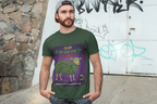 Ein Mann mit Bart und nach hinten gedrehter Kappe steht vor einer Steinmauer mit Graffiti. Er trägt ein olivgrünes T-Shirt der Marke Temple of Green Elixir mit dem Aufdruck 'Ich bin das grüne Schaf der Familie' und einem Cartoon-Schaf, dessen Wolle aus Hanfblättern besteht