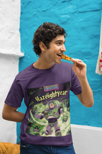 Ein junger Mann mit lockigem Haar trägt ein lila Baumwoll-T-Shirt mit dem "Hazelightyear"-Druck Illuminati Lost Seeds T-shirt﻿ von Temple of Green Elixir. Er lächelt und isst gerade einen Snack, während er vor einer leuchtend blauen Wand steht. Das T-Shirt zeigt eine humorvolle Parodie eines Weltraum-Helden inmitten von Cannabis-Blättern, was einen ironischen Kontrast zur alltäglichen Szene bildet.