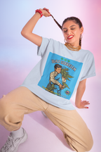 Eine junge Frau mit verspielten Zöpfen und goldenen Ketten kombiniert das hellblaue Wahre Liebe T-Shirt mit dem humorvollen 'Igaz Szerelem'-Motiv zu einer lässigen beigen Hose. Ihr selbstbewusster, fröhlicher Ausdruck unterstreicht perfekt die ironische Botschaft des Designs, das eine liebevolle Umarmung zwischen einem Mann und einer Cannabis-Frau im Retro-Stil zeigt.﻿