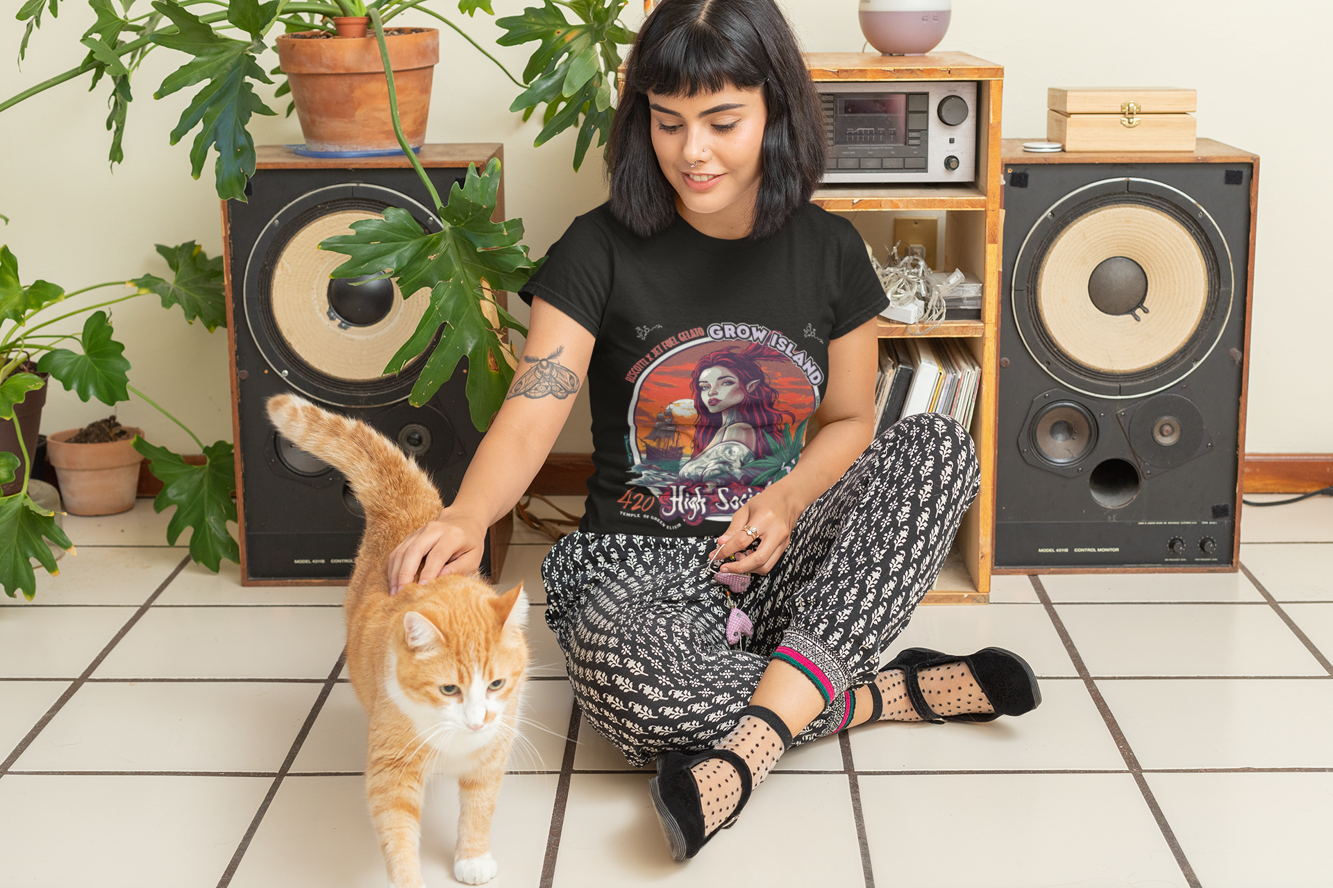 Ein schwarzhaariges Mädchen sitzt auf dem Boden vor Lautsprechern, streichelt ihre rote Katze und trägt ein schwarzes High Society T-Shirt, auf dem Folgendes zu sehen ist: Am Horizont, in den Rot- und Orangetönen des Sonnenuntergangs, nähert sich ein altes Segelschiff, während am Ufer eine Meeres-Sirene mit langem, feuerrotem Haar und spitzen Ohren steht – in ihrem Blick liegen alle Geheimnisse des Meeres. Neben ihrem Arm symbolisieren Cannabisblätter und feiner Rauch die Genüsse des Lebens und das Gefühl.