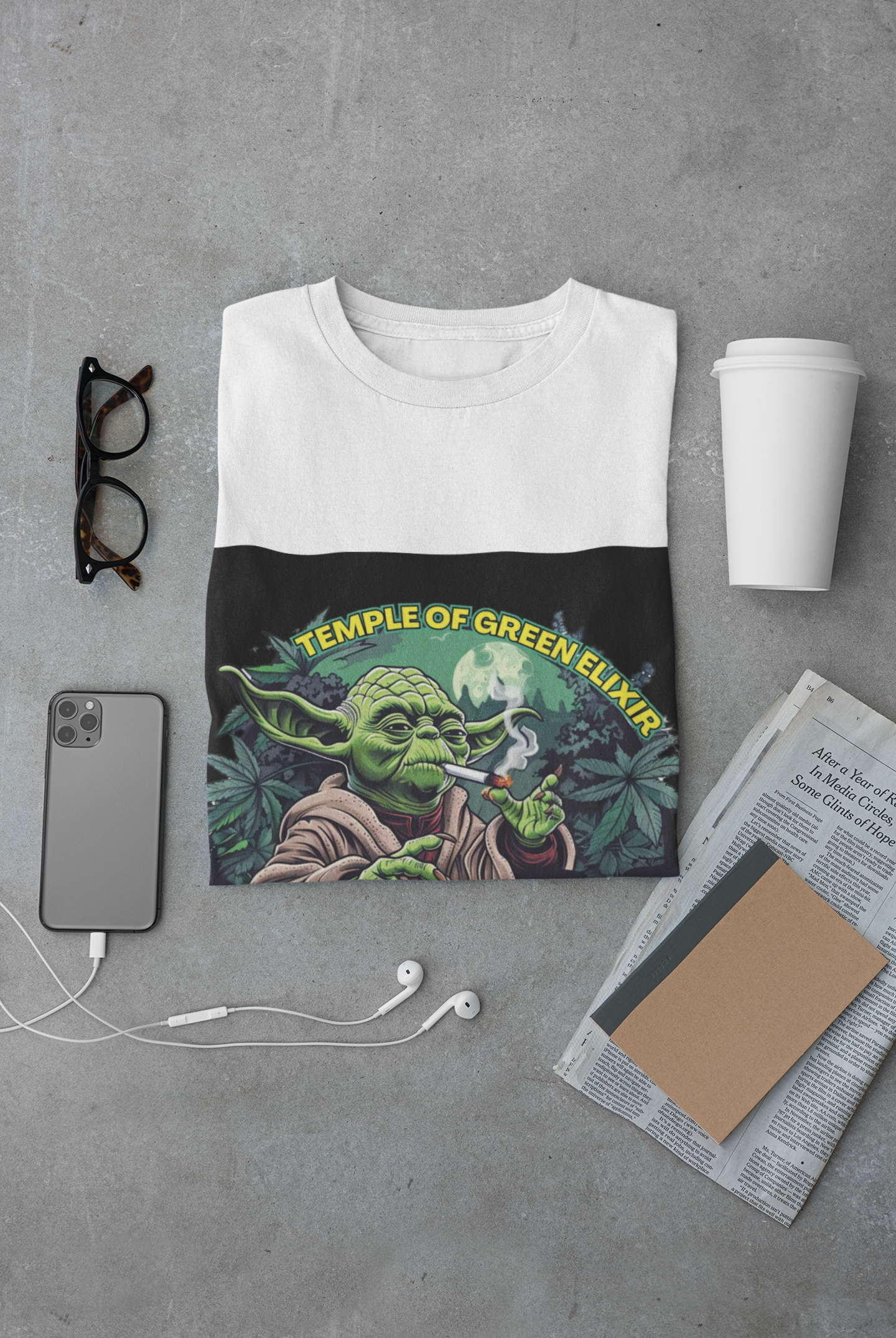 Neben einem gefalteten weißen  Imperium X T-Shirt sind vor einem grauen Hintergrund eine Brille, ein Telefon mit Kabelkopfhörern, ein Kaffeebecher, eine Zeitung und ein Notizbuch zu sehen.