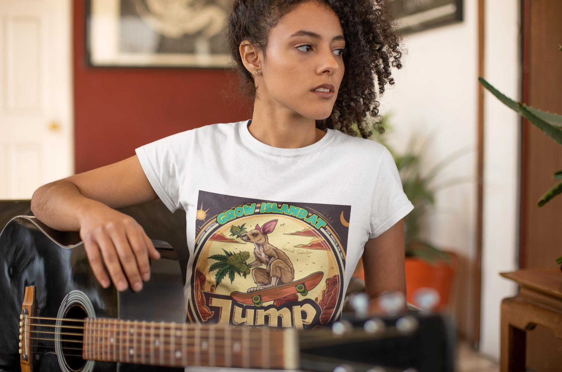 Eine gitarrenspielende Frau mit lockigem Haar trägt ein weißes Jump shot T-Shirt.  Im Mittelpunkt der Grafik steht ein skateboardfahrendes Känguru, das stolz einen frischen, harzreichen Cannabiszweig in der Pfote hält. Die roten Felsen im Hintergrund und die warmen Töne des Wüstensonnenuntergangs rufen das Gefühl von Freiheit und den wilden Westen wach. 