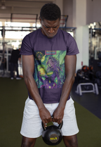 Mann hält im Fitnessstudio eine Kettlebell vor sich in lila KushBlast Kush T-shirt. Auf dem T-shirt, Frau in lila Superheldenkostüm mit gelbem ‚KUSH‘-Schriftzug hält einen grünen Becher mit der Aufschrift ‚KushBlast‘ vor grünem, psychedelischem Hintergrund. Oben erscheint ‚Illuminati Lost Seeds‘ und ‚Temple of Green Elixir Limited Edition‘