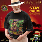 Älterer Mann mit Strohhut trägt ein schwarzes T-Shirt mit Mr. Blunti-Motiv, vor rotem Sonnenuntergang, umgeben von Schriftzügen wie ‚Illuminati Lost Seeds‘, ‚Temple of Green Elixir‘ und dem Slogan ‚Stay Calm Go High‘. Auf dem Tshirt steht ein Mann im Anzug hält einen brennenden Joint und sitzt neben einem lächelnden Teddybär in rauchgeschwängerter, grüner Umgebung. Oben steht ‚Temple of Green Elixir Limited Edition‘, unten der Schriftzug ‚MR. BLUNTI‘ und das Illuminati Lost Seeds Logo.