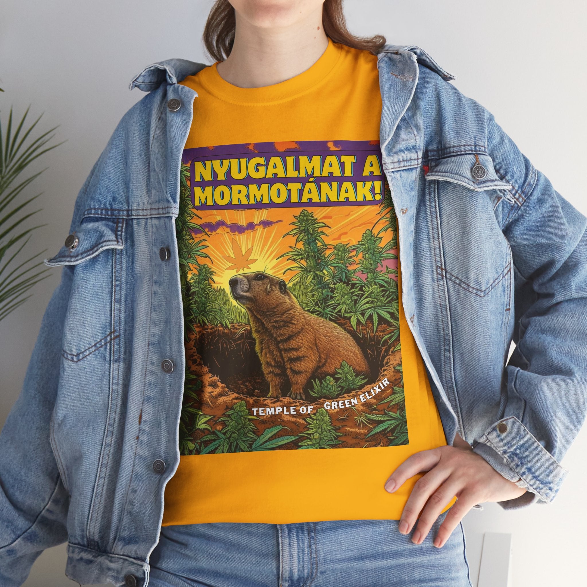 Model trägt Jeans Jacke und Nyugalmat a Mormotának gelbes T-shirt. Ein Murmeltier sitzt inmitten vieler grüner Pflanzen auf einem Feld, im Hintergrund Sonnenstrahlen und lila-orangefarbener Himmel. Oben steht der gelbe Text ‚NYUGALMAT A MORMOTÁNAK!‘, unten der Schriftzug ‚TEMPLE OF GREEN ELIXIR‘.