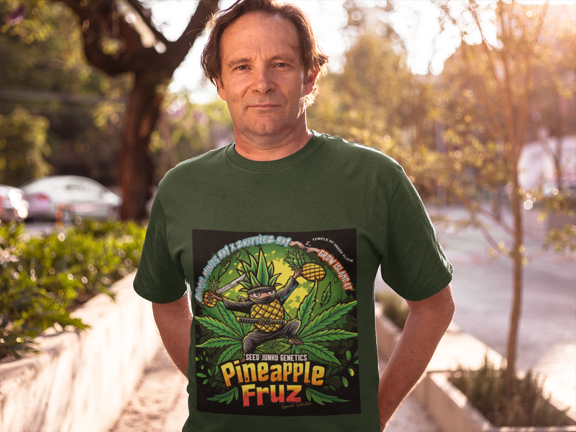 Mann zwischen 50 und 60 Jahren steht auf der Straße mit den Händen in den hinteren Taschen, trägt ein grünes Pineapple Fruz T-Shirt. Auf dem T-Shirt lässige Ananas-Ninja-Figur mit einem leuchtenden Katana und hoch erhobener frischen Ananas im Hintergrund sind üppige Cannabisblätter zu sehen.