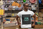 Ein Mann steht und lehnt sich in einem Plattenladen vor CDs und Büchern an. Er trägt eine schwarze Sonnenbrille und ein weißes Signature Pattern Tee T-Shirt. Schwarzer Hintergrund mit einer fließenden, wiederholenden Logostruktur, in der Mitte ein ikonischer türkisfarbener Block mit Temple of Green Elixir Schrift.