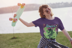 Eine junge Frau mit Sonnenbrille und Skateboard in der Hand genießt einen sonnigen Tag. Sie trägt das lila Dementhol T-Shirt, lässig kombiniert mit einem offenen Karohemd. Ihr fröhliches Lächeln und der entspannte Skater-Vibe bilden einen humorvollen Kontrast zum schaurigen Geister-Motiv des Shirts. Diese limitierte Edition von Temple of Green Elixir ist der perfekte Begleiter für alle, die ihren einzigartigen Stil mit einem Augenzwinkern zeigen.