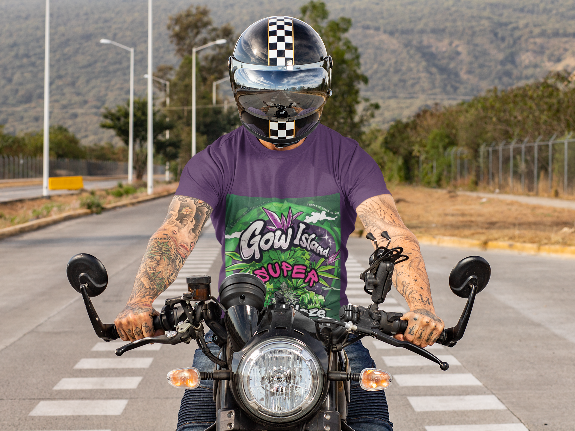 Ein tätowierter Junge sitzt auf einem Motorrad in der Straßenmitte, trägt einen Helm, vor einem schönen grünen Hügel als Hintergrund. Er hat ein lila Super Silver Haze T-Shirt an, mit Leuchtende Grün- und Lilatöne, detailreiche Cannabis-Pflanzenmotive und markante Typografie