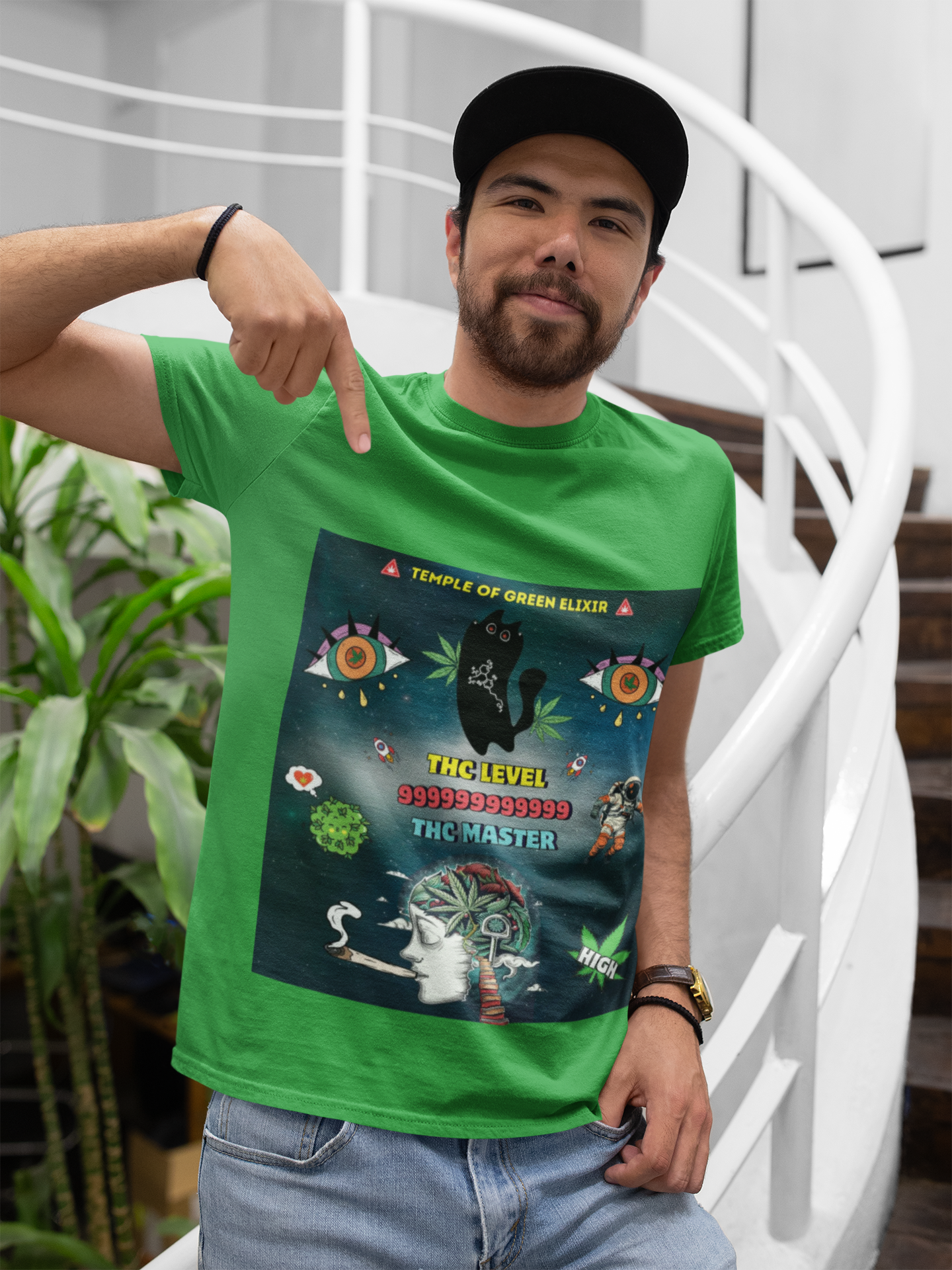 Mann mit grünem T-Shirt, das ein psychedelisches Design zeigt: große bunte Augen, schwarze Katze vor Hanfblatt, Astronaut, galaktischer Hintergrund, Gehirn-Motiv, Rauch, Schriftzüge „Temple of Green Elixir“, „THC LEVEL 999999999999“, „THC MASTER“ und „HIGH“, stehend auf einer Treppe in einem modernen Innenraum mit Pflanzen.