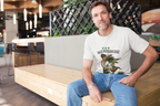 Ein Mann sitzt entspannt auf einer hellen Holzbühne in einem modernen Café oder Restaurant. Er trägt ein weißes T-Shirt mit der Aufschrift „IGAZ SZERELEM“ und einer Illustration, auf der eine Person eine große Cannabispflanze umarmt. Über der Grafik sind drei kleine Hanfblätter zu sehen. Der Mann schaut freundlich in die Kamera, im Hintergrund befinden sich Tische, Stühle und hängende Lampen. Die Szene wirkt ruhig, natürlich und stilvoll.