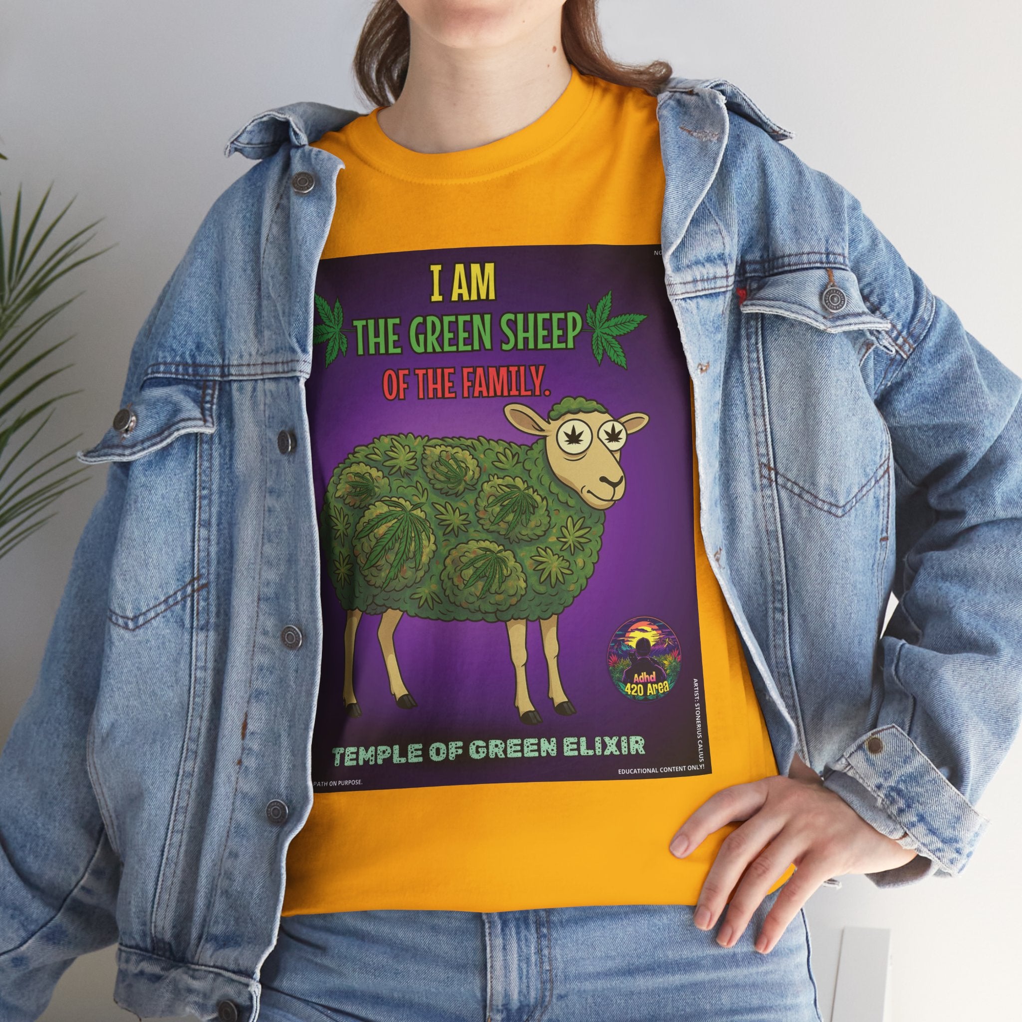 Model steht in jeans Jacke und gelbem T-shirt mit Design des The Green Sheep: Ein Schaf, dessen Fell vollständig aus Cannabisblättern geformt ist. Darunter steht der Markenname 'Temple of Green Elixir'.﻿