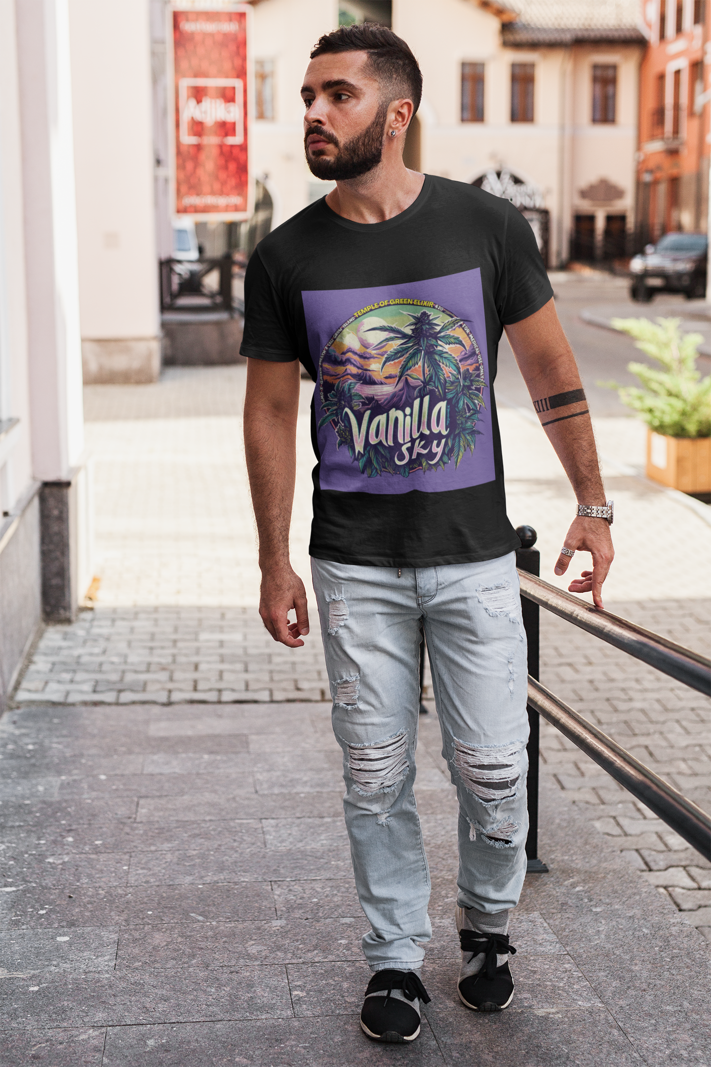 Ein junger Mann spaziert auf der Straße und trägt ein schwarzes Vanilla Sky T-Shirt mit Kreatives Cannabis-Design mit tropischem Inselmotiv und lila Himmel, großer „Vanilla Sky“-Schrift, Cannabispflanzen im Vordergrund, Sonnenuntergang und Palmen – medizinische Sorte GMO x Garlic Breath x Cali Grow Island von Grow Island.