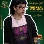 Tatowierte Dame trägt schwarze Brille, ein hellrosa T-Shirt mit Vaticaan Archives-Motiv und schwarzer Strickjacke, vor grünem Hintergrund mit Schriftzügen wie ‚Illuminati Lost Seeds‘, ‚Temple of Green Elixir‘ und ‚The real secret hides in the terpene‘. Auf dem T-shirt  gotische Figur, umgeben von lilafarbenen und grünen Cannabisblättern. Auf ihrem Kopf thront eine provokative Krone mit Kreuzmotiv. 