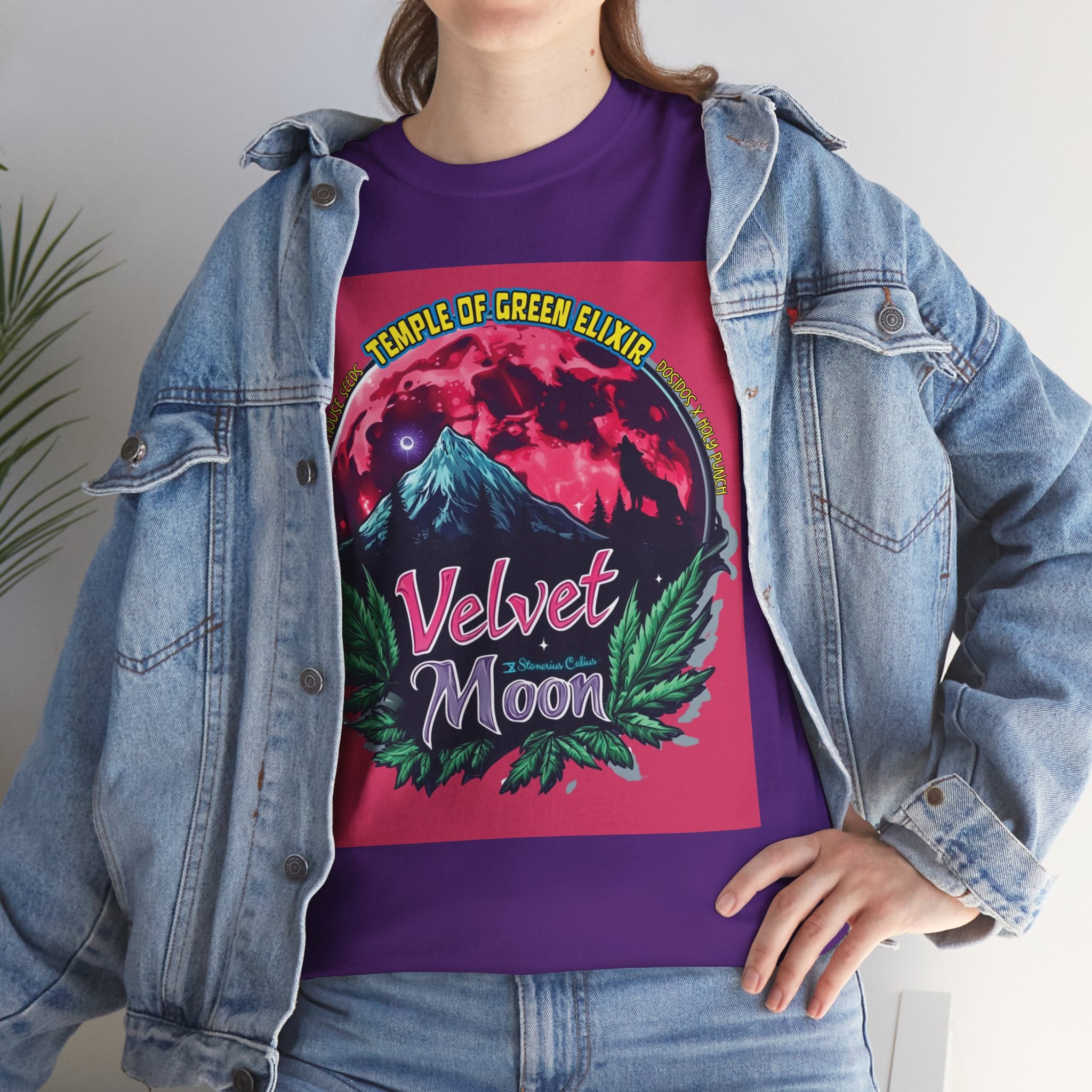 Model steht im Jeans Jacke und lila Velvet Moon T-shirt.  Die Grafik erzählt von einer besonderen Nacht, in der das samtige Licht des blutroten Mondes die Berggipfel umhüllt und ein einsamer Wolf in den Schatten der dunklen Wälder hineinheult. Die Luft ist erfüllt vom Duft der frischen Bergluft, die die Freiheit der Wildnis und den Zauber des Unbekannten mit sich bringt. Cannabisblätter rahmen die Szene ein, als würde die Natur selbst diesen geheimen Moment beschützen. 