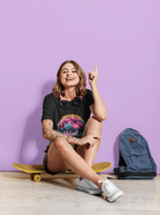 Eine Frau sitzt auf einem gelben Skateboard vor einem lila Hintergrund, rechts von ihr ein blauer Rucksack, sie trägt ein schwarzes Velvet Moon T-Shirt. Die Grafik erzählt von einer besonderen Nacht, in der das samtige Licht des blutroten Mondes die Berggipfel umhüllt und ein einsamer Wolf in den Schatten der dunklen Wälder hineinheult. Die Luft ist erfüllt vom Duft der frischen Bergluft, die die Freiheit der Wildnis und den Zauber des Unbekannten mit sich bringt. Cannabisblätter rahmen die Szene ein.