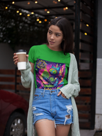 Eine Frau trägt ein grünes Wubba Luba Bud T-Shirt von Illuminati Lost Seeds und Temple of Green Elixir. Das farbenfrohe, psychedelische Design zeigt eine futuristische Katze mit Cannabisblüten in der Hand. Sie kombiniert das Shirt mit Jeansshorts und einem hellgrünen Cardigan, während sie einen Kaffeebecher hält – ein lässiger Streetstyle mit urbanem Flair.