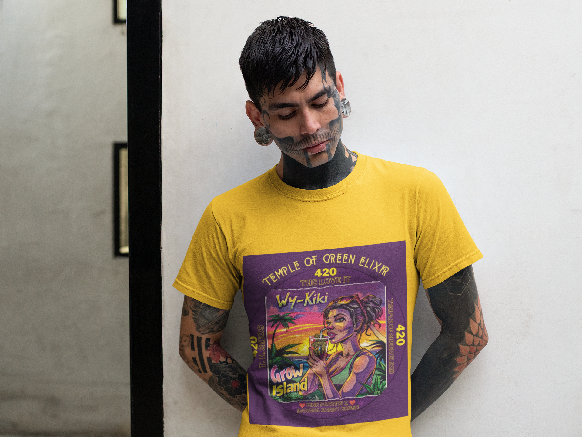 Tatowierte Mann steht vor der Wand im Wy-Kiki gelbes T-shirt, Am Horizont versinkt die Sonne langsam im Meer, die Schatten der Palmen werden lang, und in der Luft liegt der Duft von Salz, Früchten und frisch getrockneten Cannabis Blüten. Im Mittelpunkt steht eine entspannte, stilvolle Frau, die an einem exotischen Drink nippt – darin schwimmen keine Zitronen oder Limetten, sondern kleine, perfekte Cannabis Buds, als würde sie die Essenz des Sommers trinken. 